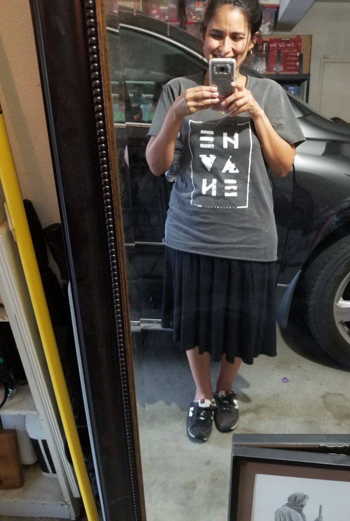 Geri in mismatched clothes, taking a mirror selfie in the garage